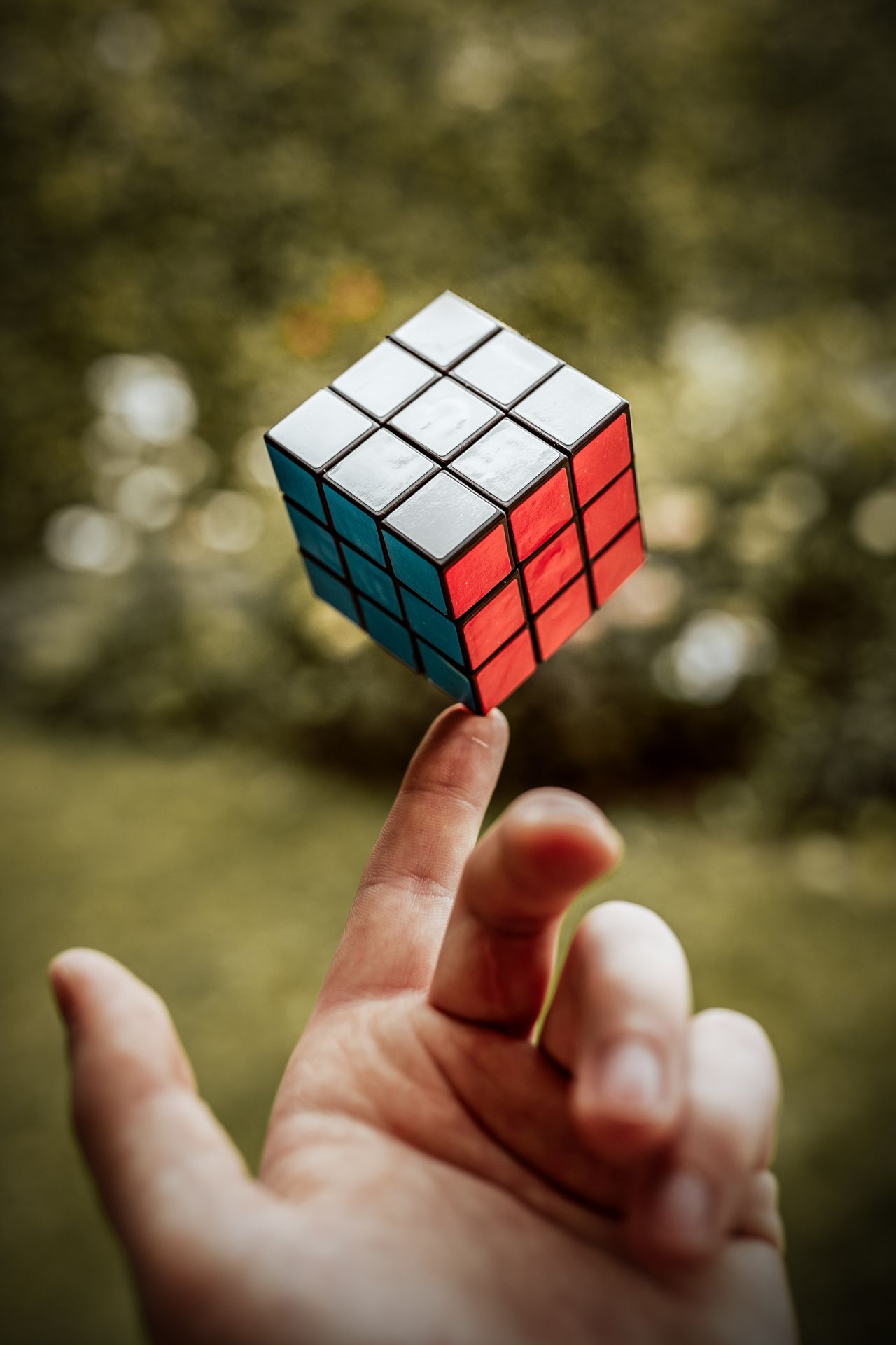 A Rubik's Cube balanced on a fingertip outdoors, showing its white, blue and red faces
